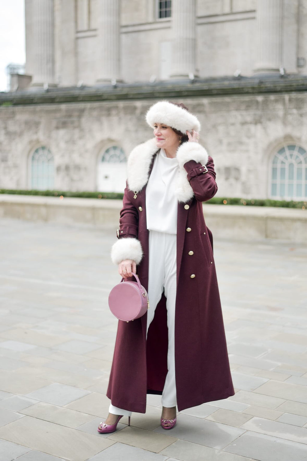 A woman stood in a purple outfit with a round leather handbag 