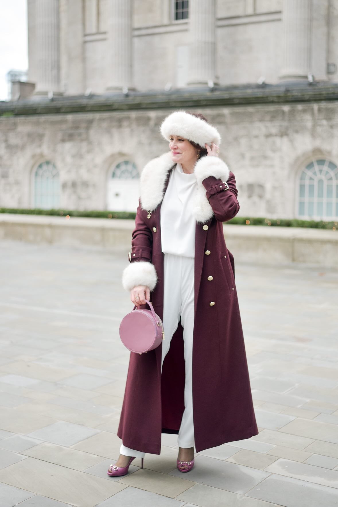 A woman stood in a purple outfit with a round leather handbag 