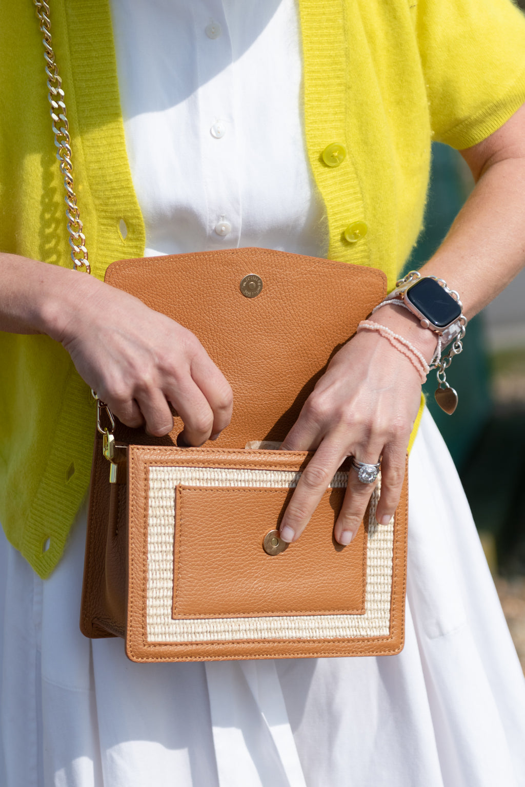 Person holding a tan raffia leather handbag with a yellow cardigan and white dress made it Italy Independence UK label 