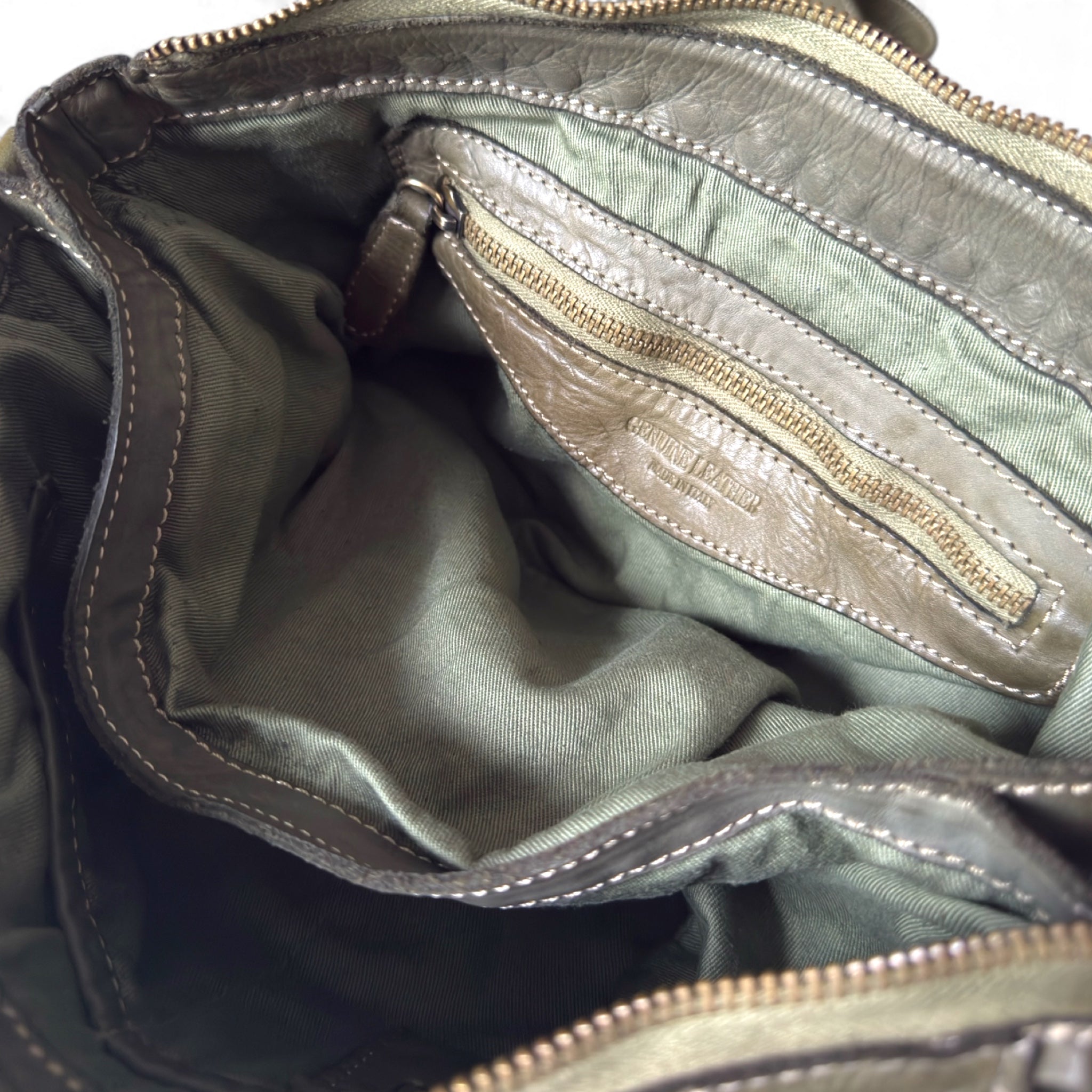 Showing an inside zipped pocket of an olive green handwoven Italian leather pouch 