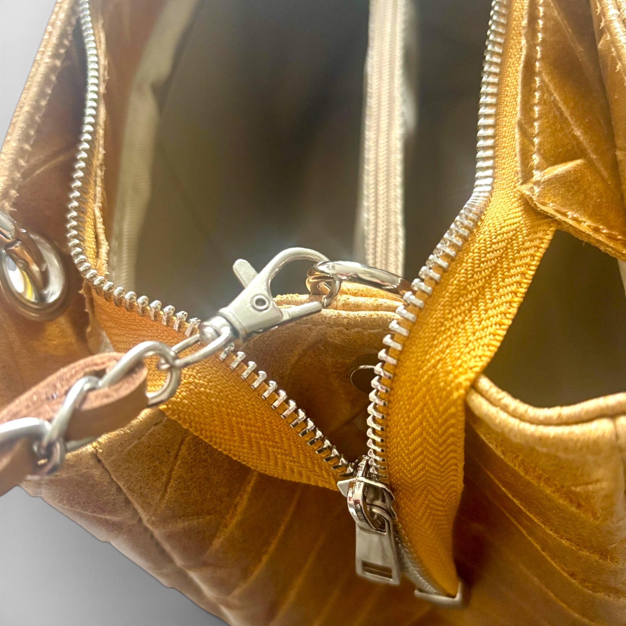 Close-up of a mustard yellow leather bag with a silver zipper and chain detail.
