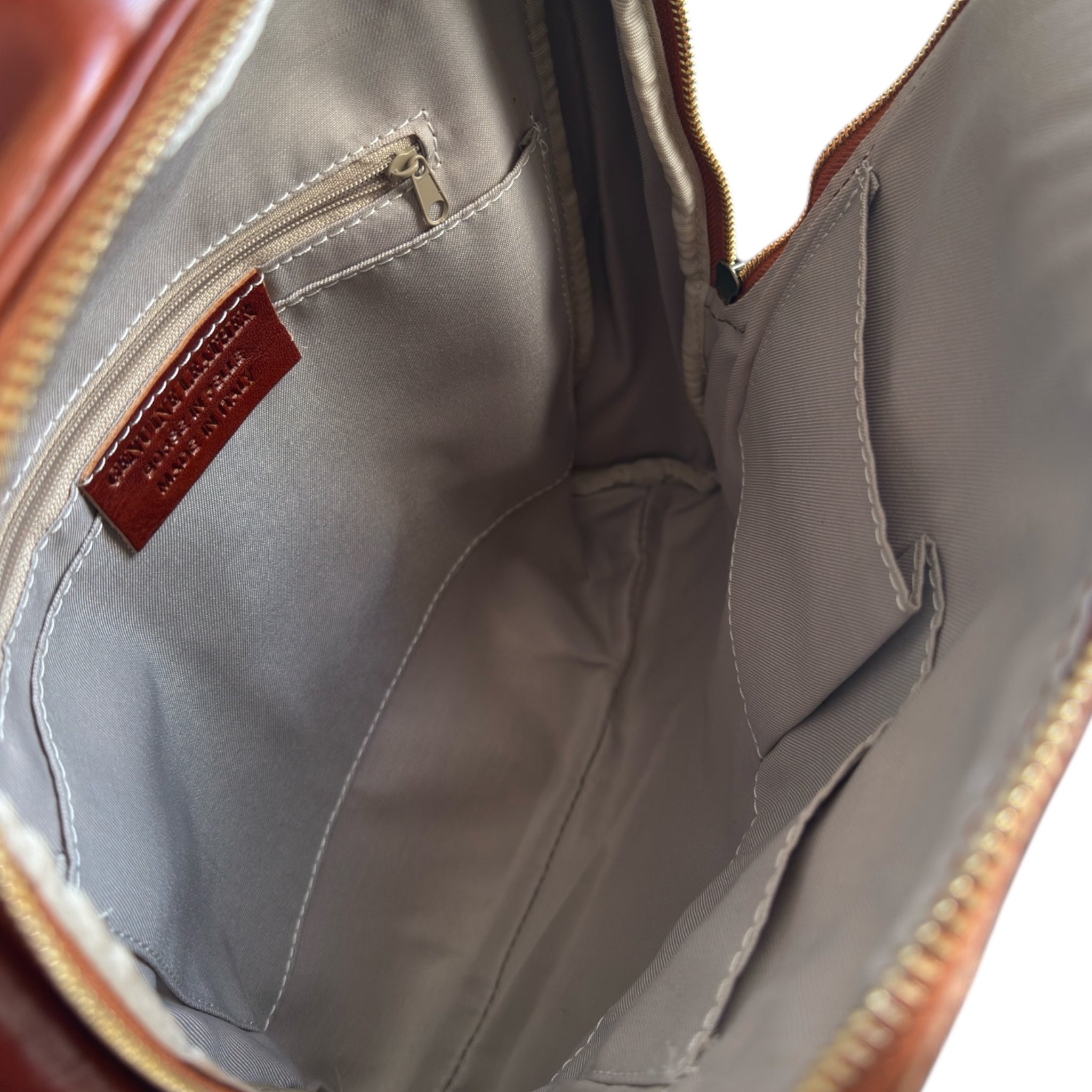 Close-up of an open tan leather backpack bag with a zipper, showing the interior.