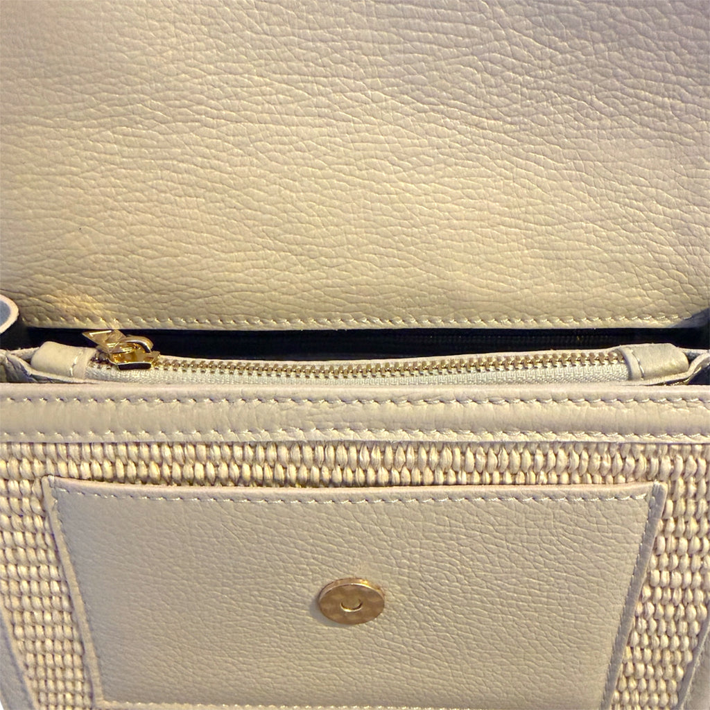 Close-up of a light-colored  cream leather handbag with a gold zipper and clasp.