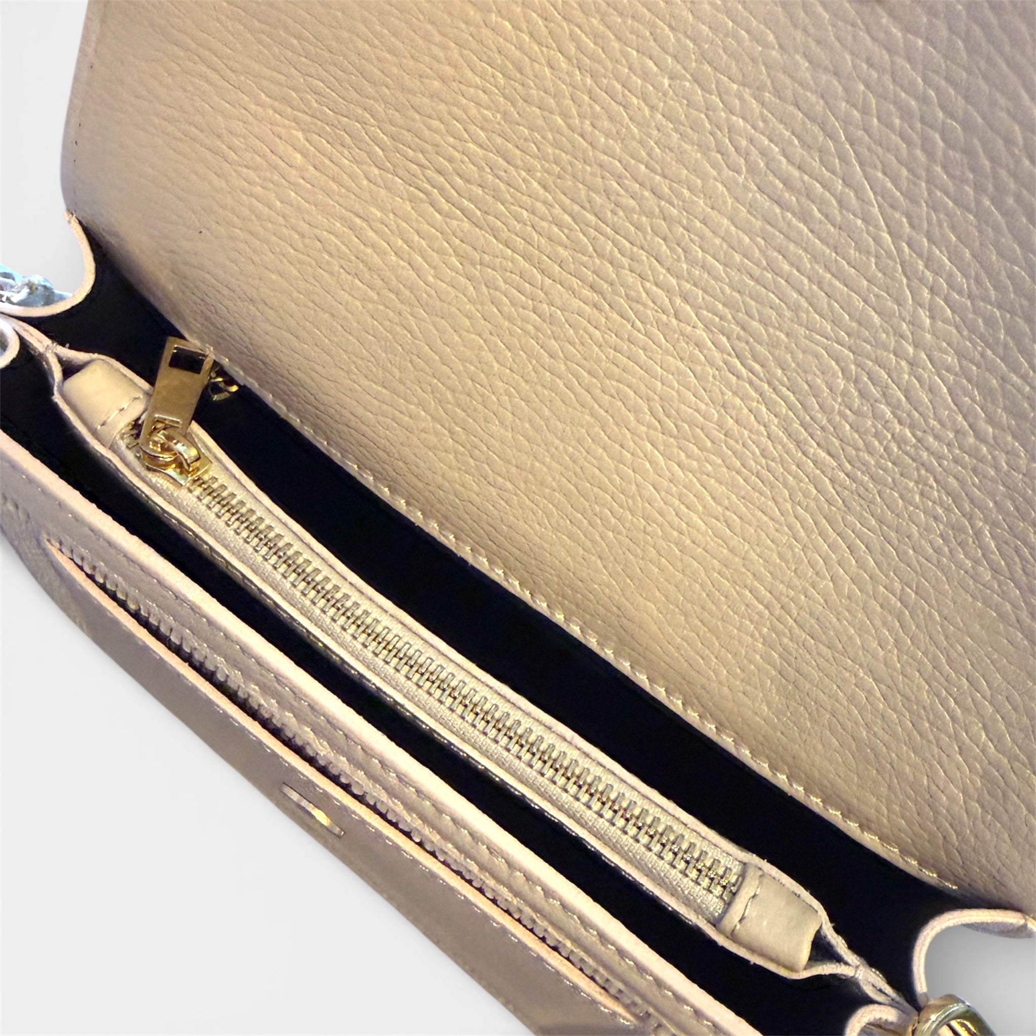 Close-up of a cream handbag with gold zipper and hardware on a light gray background